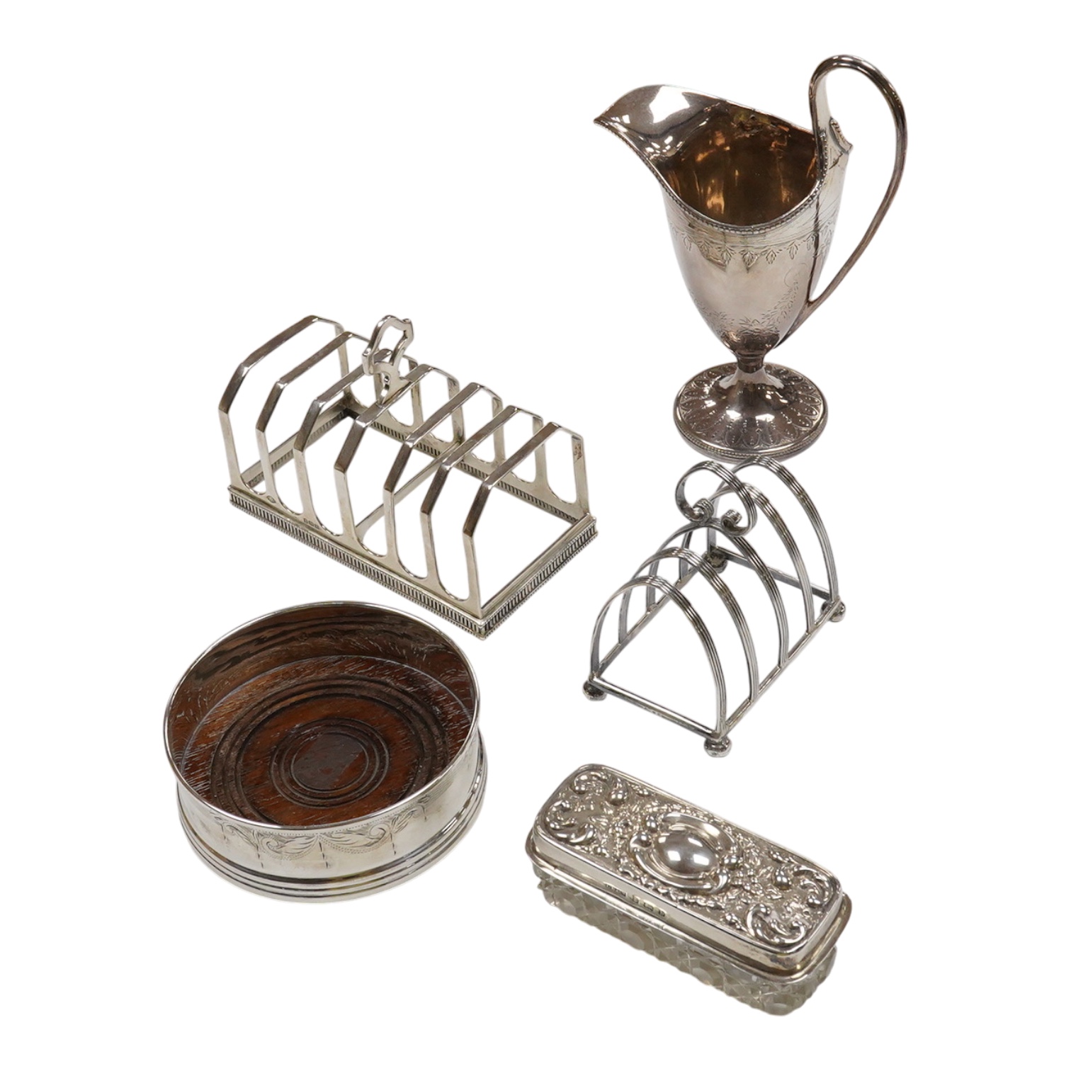 A George III engraved silver helmet shaped cream jug, Henry Chawner, London 1788(repair), height 15.3cm, together with two George V silver toast racks, a silver mounted glass toilet jar and a modern silver mounted bottle